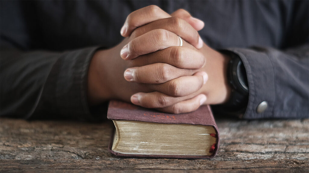 person praying with their hand on the bible